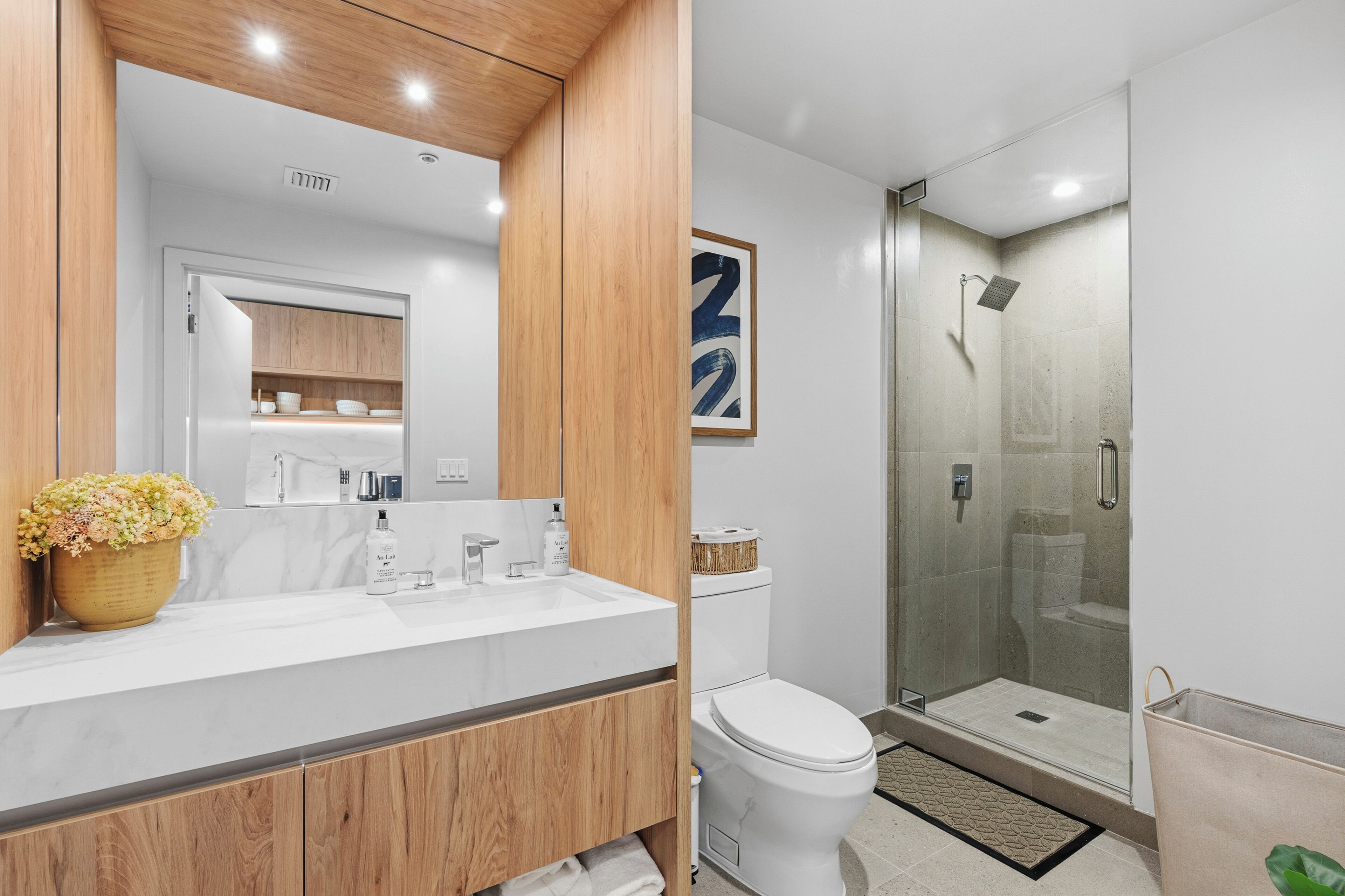 Un baño moderno con tocador de madera, un espejo grande, cabina de ducha y un inodoro.