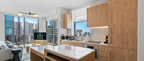A modern kitchen with wooden cabinets, a central island, and a large window offering a city view.