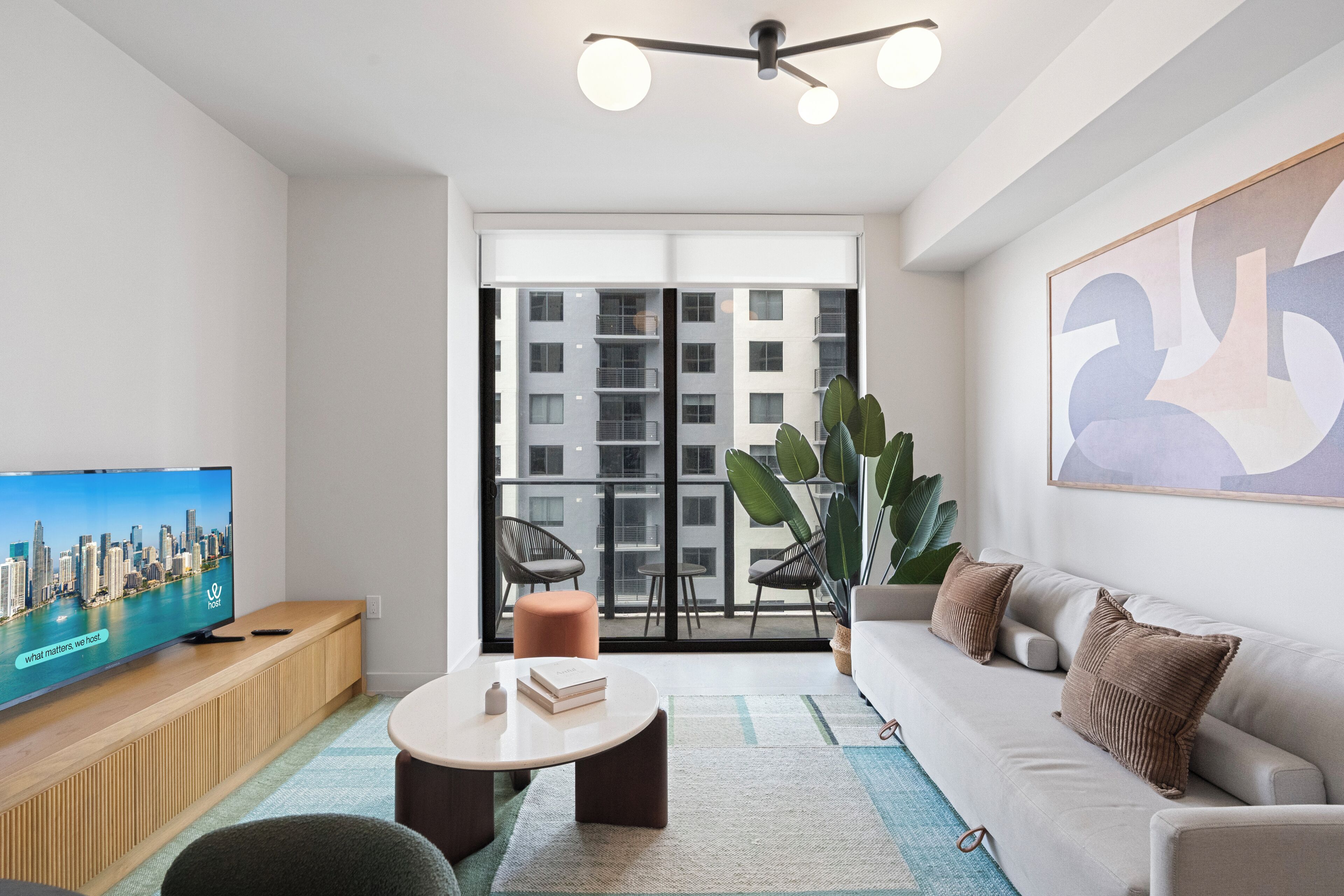 Una sala de estar moderna con un televisor de pantalla plana, un sofá, una mesa de centro y un balcón con vistas a la ciudad.