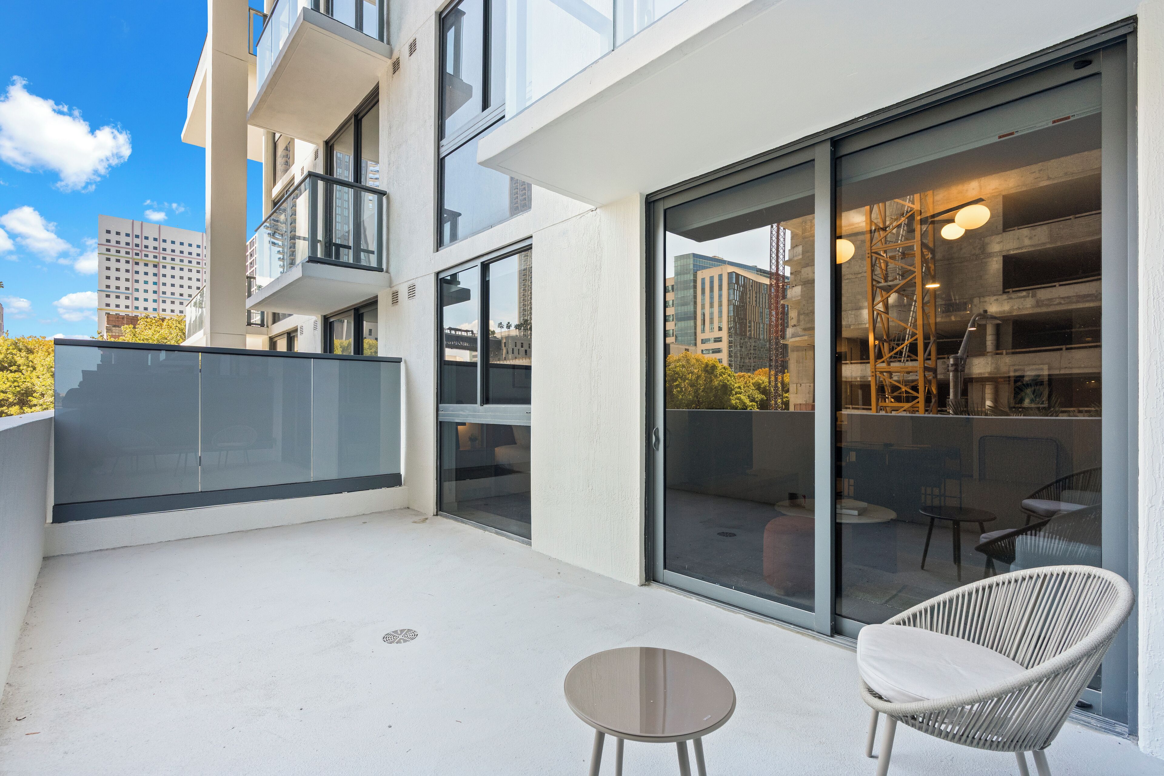 A modern balcony with glass doors, a wicker chair, and a small table.