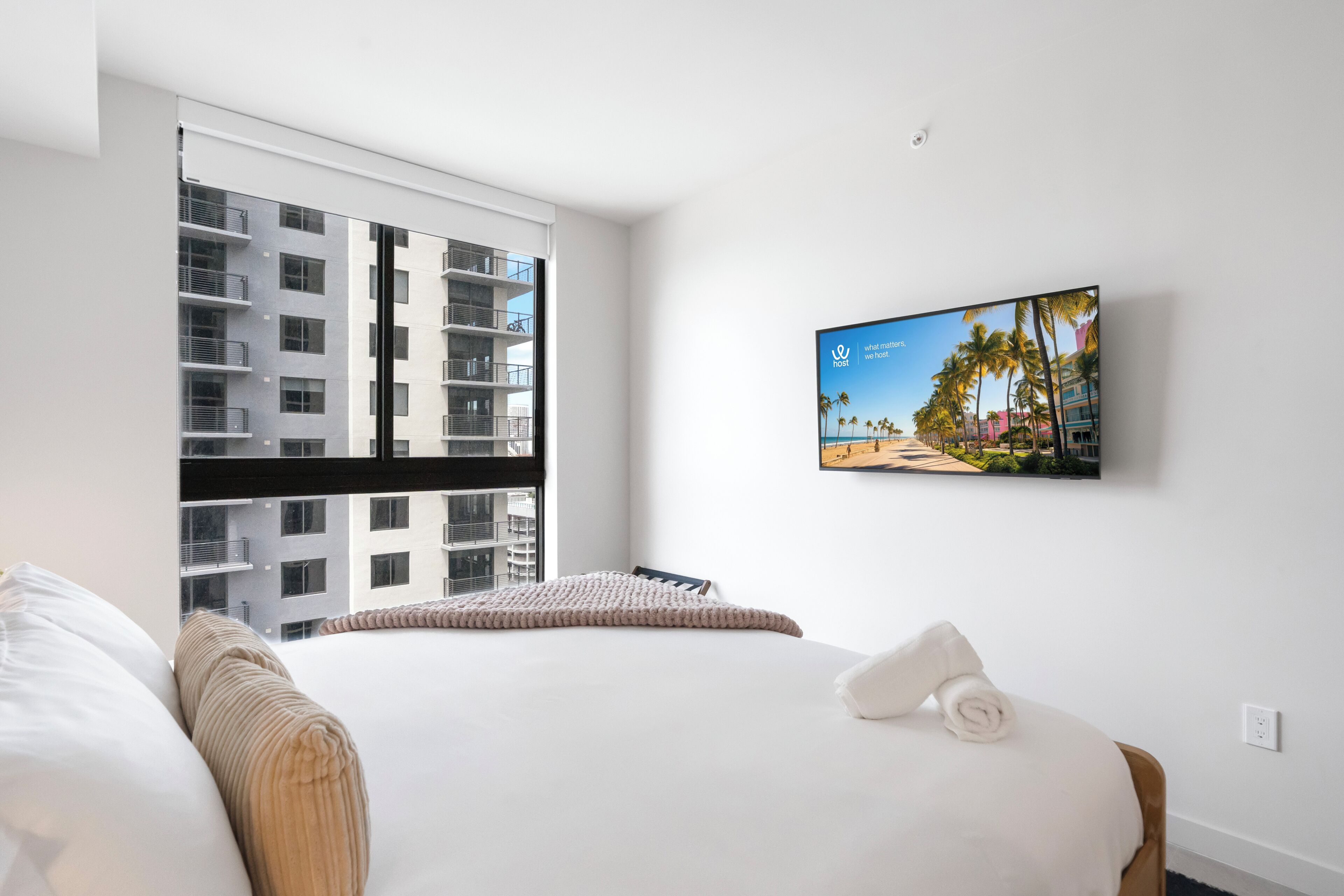 Une chambre d’hôtel avec un lit, une fenêtre donnant sur un immeuble et un téléviseur fixé au mur.