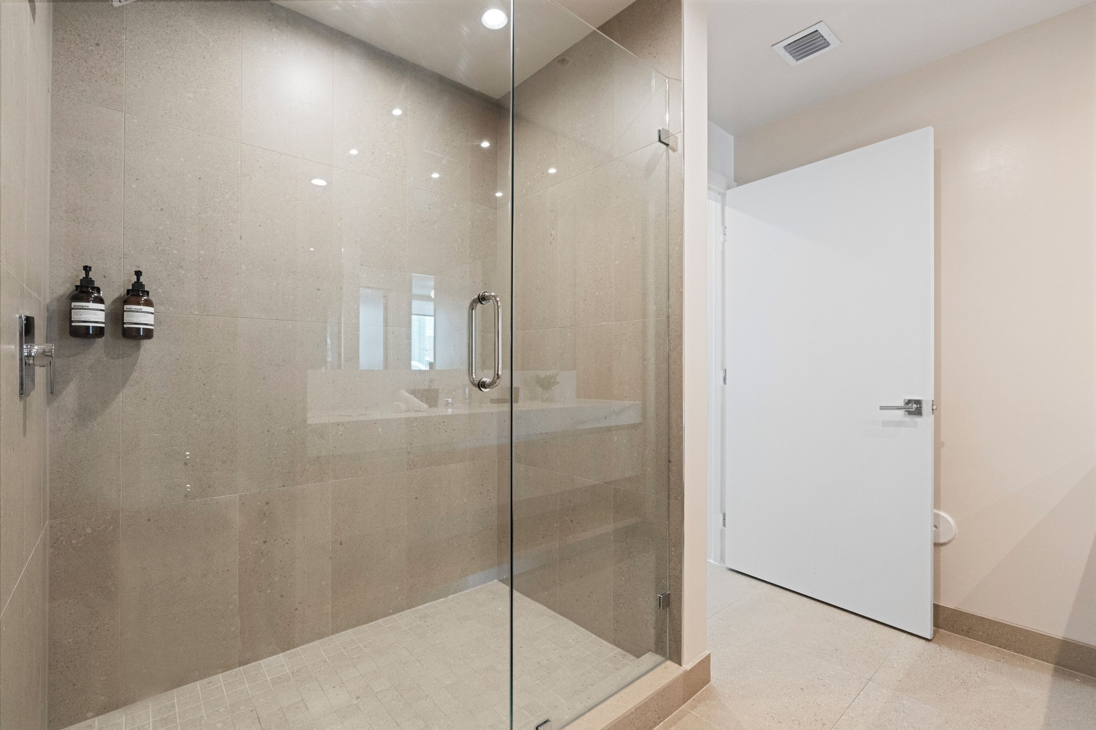 A modern bathroom with a glass-enclosed shower, a white door, and two soap dispensers on the wall.