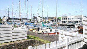 Un port de plaisance où sont amarrés de nombreux voiliers, une passerelle en bois et des bâtiments en arrière-plan.