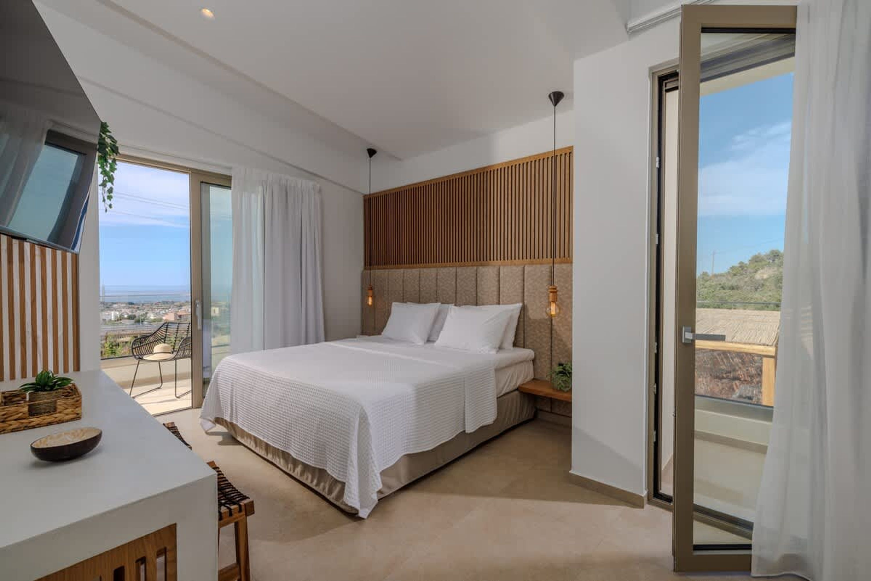 A modern bedroom with a large bed, a desk, and a balcony with a view.