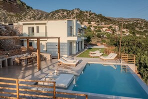 En moderne villa med swimmingpool, udendørs møbler og udsigt over de omkringliggende bakker.