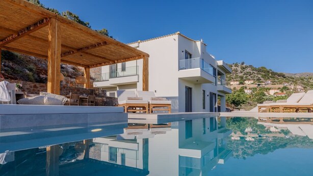 Eine moderne Villa mit Pool, Sitzgelegenheit im Freien und Blick auf die Hügellandschaft.