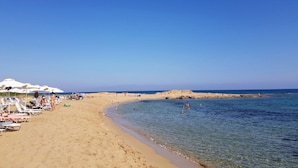 Ein Strand mit weißen Sonnenschirmen, Liegestühlen und klarem, blauem Wasser.
