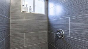 A bathroom with a modern design, featuring a shower with a wall-mounted faucet and a window above the sink area. - Marbella Lane - Adorable and Quiet Studio (San Mateo)