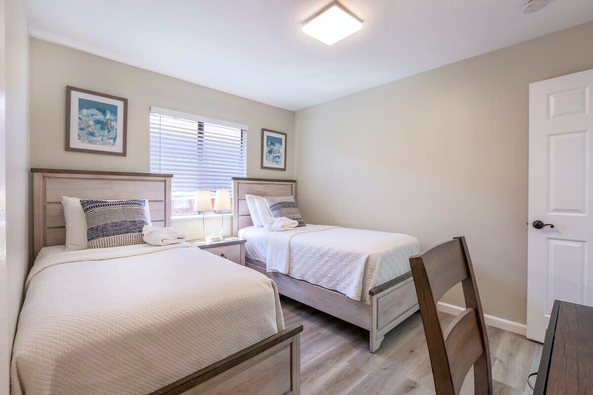 Een slaapkamer met twee bedden, een stoel, een bureau en een deur.