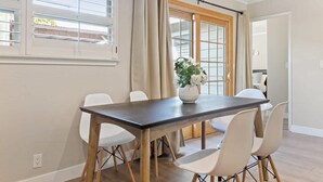 Un'area pranzo con un tavolo in legno scuro, sedie bianche e un vaso con fiori.