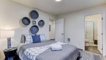Un dormitorio ordenado con una cama grande, una mesita de noche, una lámpara de pared y una puerta que da a un baño.