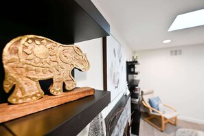 A wooden elephant sculpture on a black shelf in a modern living room with a white wall and a blue chair in the background. - Marbella Lane - Exquisite Home 3BR (Sunnyvale)