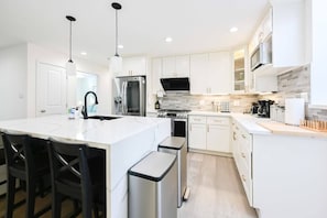 A modern kitchen with white cabinets, stainless steel appliances, and a central island with bar stools. - Marbella Lane - Exquisite Home 3BR (Sunnyvale)