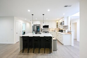 A modern kitchen with white cabinetry, a central island with bar stools, stainless steel appliances, and pendant lighting. - Marbella Lane - Exquisite Home 3BR (Sunnyvale)