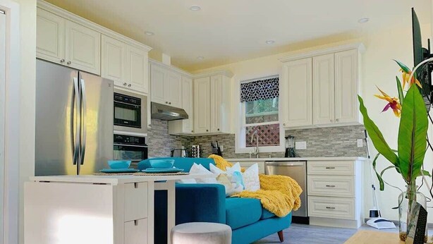 A modern kitchen with white cabinets, a blue sofa, and a wooden dining table. - Marbella Lane Cozy 2BR Studio Duplex Home (San Mateo)