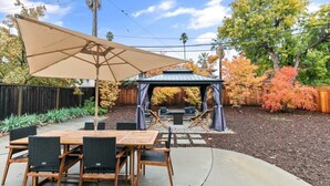 An outdoor patio with a wooden table and chairs, a large beige canopy, and a gazebo. - Marbella Lane - Modern 3BROasis in SiliconValley (San Jose)