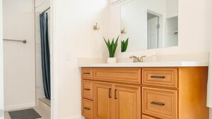 A bathroom with wooden cabinets, a white sink, and a mirror. - Marbella Lane - 4BR Alluring Home (Union City)