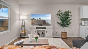 A modern living room with a flat-screen TV, a dining table, a potted plant, and a white cabinet. - Marbella Lane - Amazing 4BR Lakeview Home (Austin)