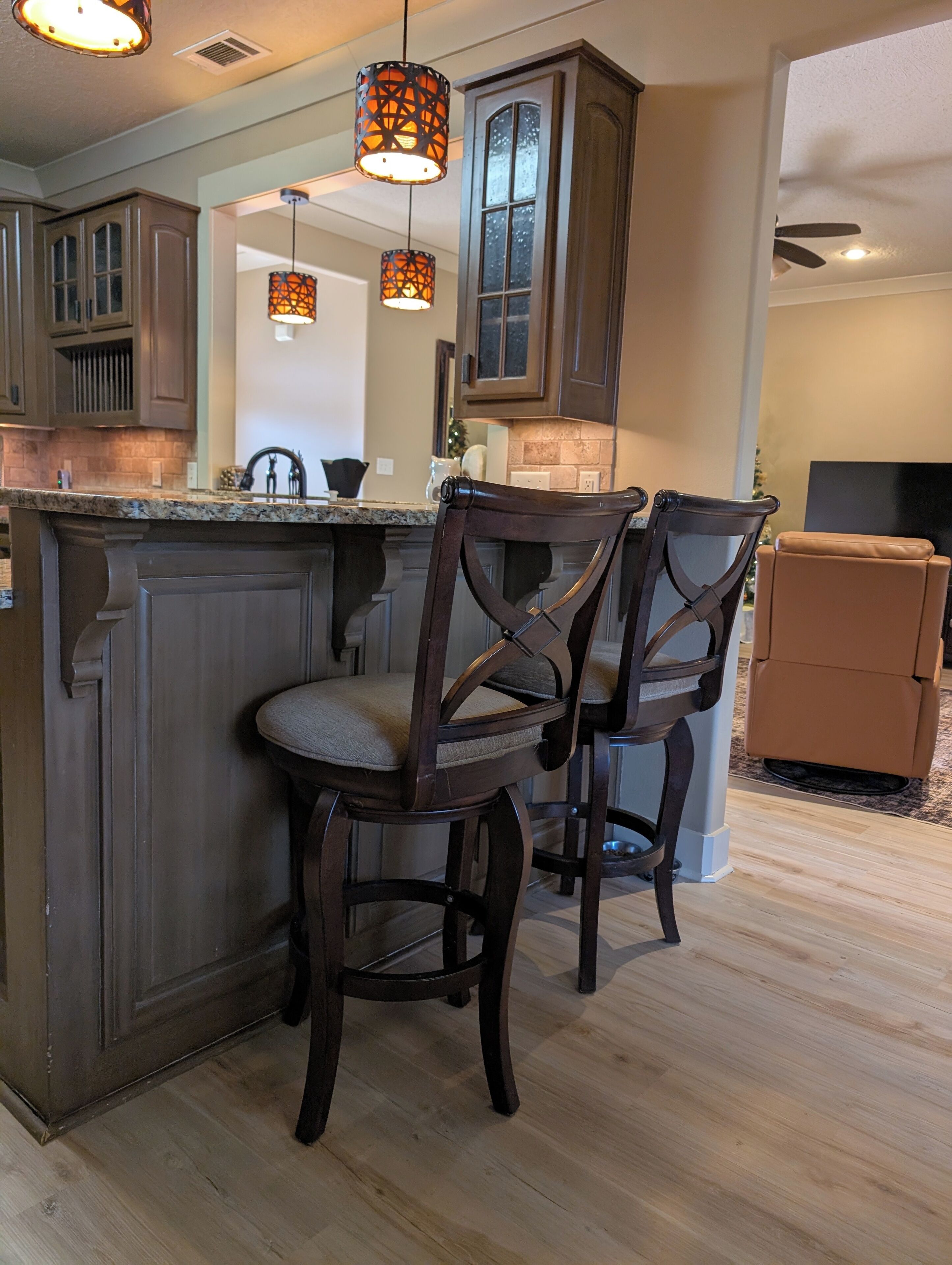 A kitchen with dark wooden cabinets, a granite countertop, and two bar stools.