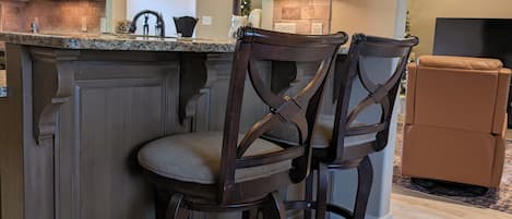 A kitchen with dark wooden cabinets, a granite countertop, and two bar stools.