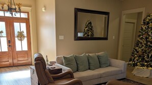 A living room with a beige sofa, a leather chair, a wooden floor, and a Christmas tree. - 2651 sqft - Fenced Backyard / Firepit / 5m to LR (Bryant)