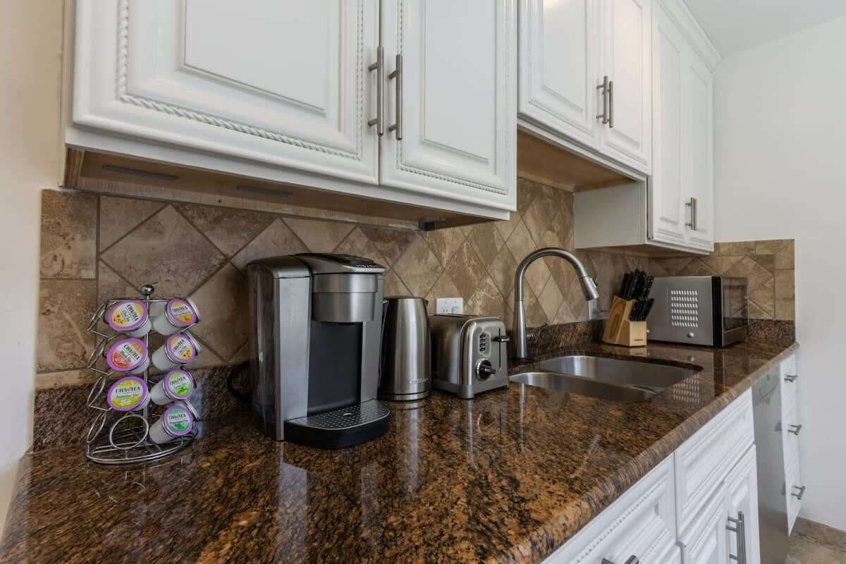 A kitchen with white cabinets, a granite countertop, a coffee maker, a toaster, and a knife block.
