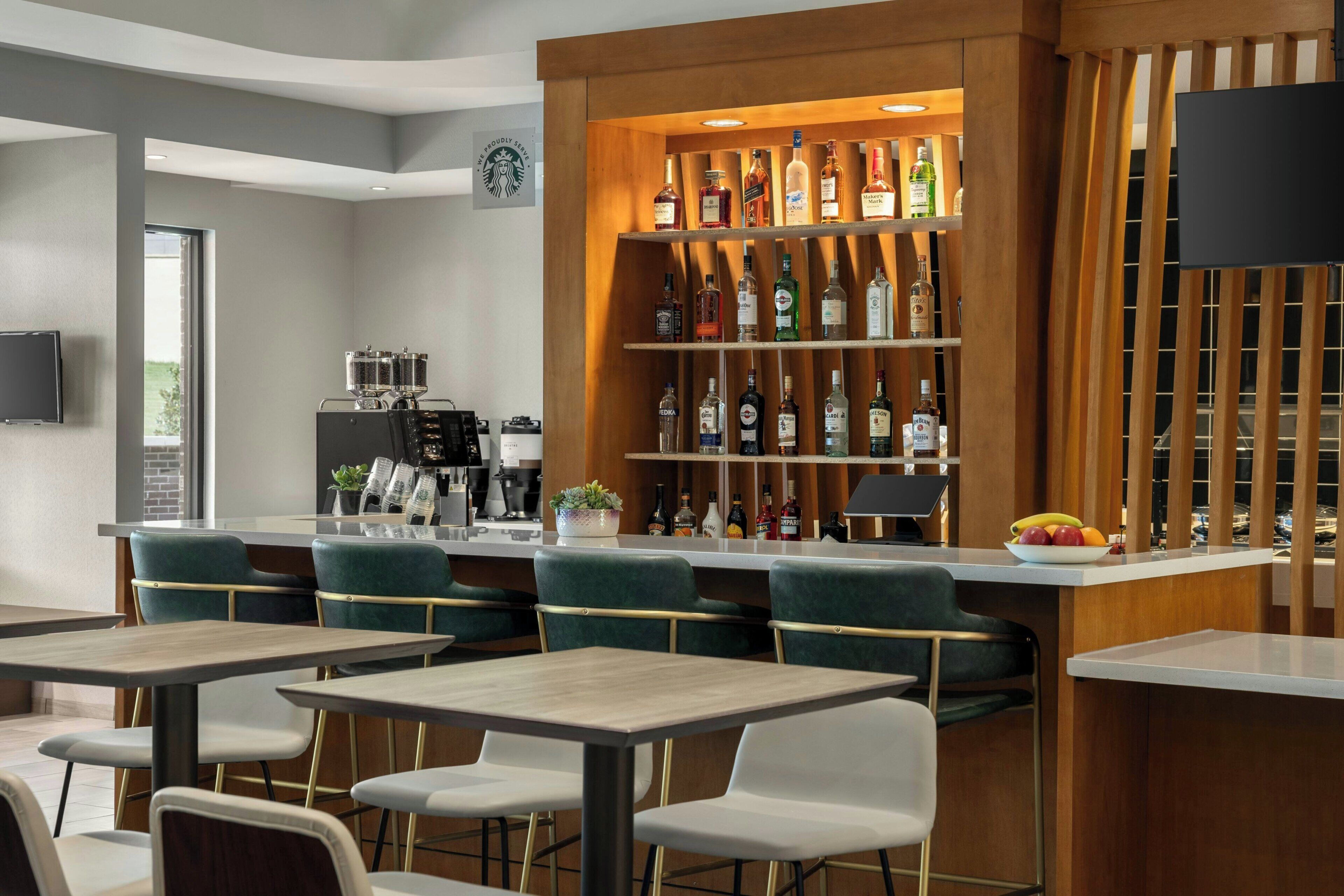 Un espace bar moderne, doté d’un assortiment de bouteilles d’alcool, d’une machine à café et de différents types de sièges.
