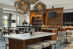 Zona de bar moderna con barra central, asientos y una variedad de botellas de licor.