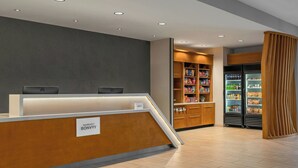Ein Hotel-Empfangsbereich mit Holztresen, einer Namensschild, einem Automaten und einem mit Getränken gefüllten Kühlschrank.