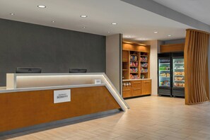 Una zona reception di un hotel con un bancone in legno, una targhetta, una macchina distributrice e un frigorifero fornito di bevande.