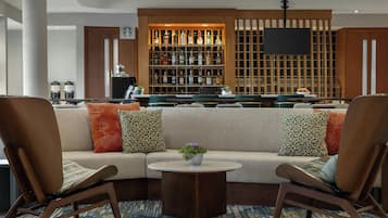 A modern lounge area with a sofa, two armchairs, a coffee machine, and a bar with various bottles.