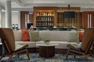 Un área de estar moderna con un sofá, dos sillones, una cafetera y una barra con varias botellas.