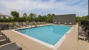 Ein rechteckiger Pool mit einer gefliesten Kante, umgeben von Liegestühlen und einer Backsteinmauer.