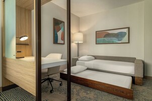 Habitación de hotel con cama, escritorio, silla, lámpara y dos cuadros abstractos en la pared.