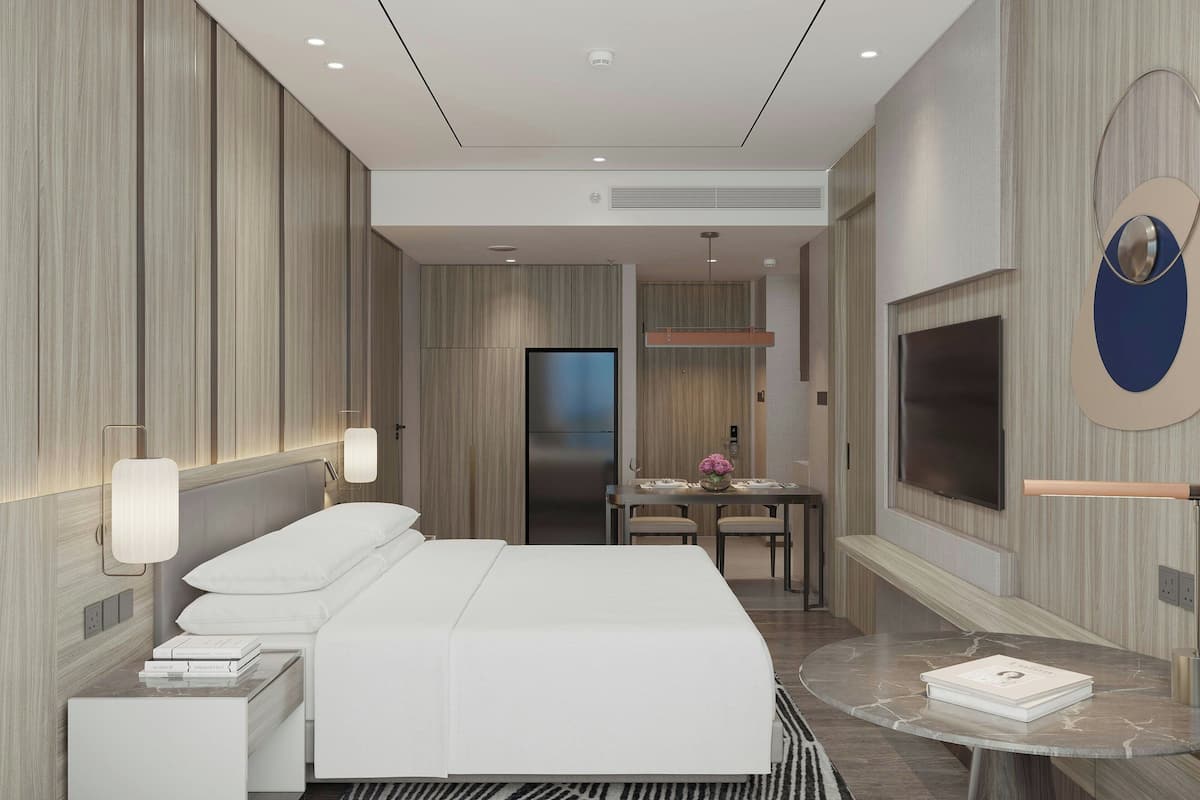 Une chambre d’hôtel moderne avec un grand lit, un coin repas et un téléviseur fixé au mur.