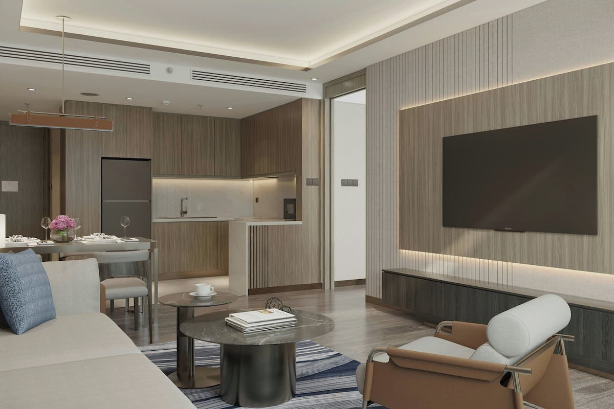 Un salon moderne avec un canapé, une table basse, un téléviseur fixé au mur et un coin cuisine à l’arrière-plan.