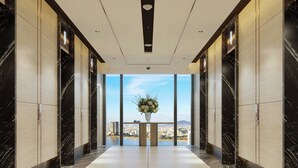 En modern hotellkorridor med marmorgolv, stora fönster och utsikt över stadsbilden.