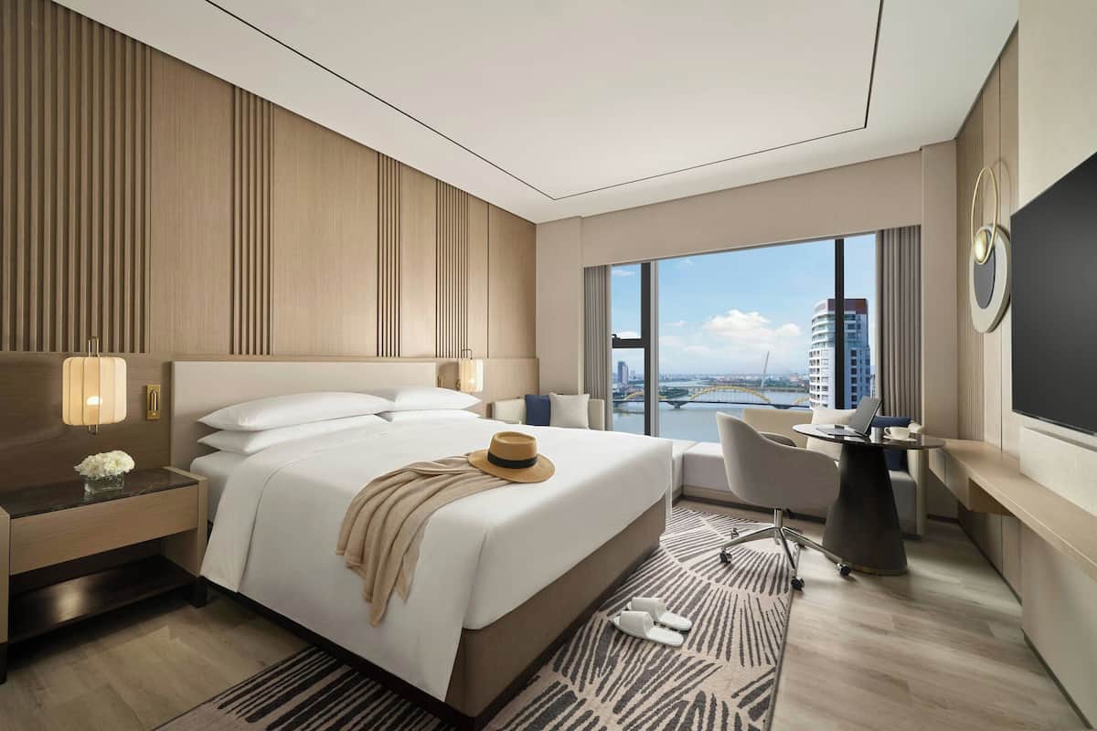 Une chambre d’hôtel moderne, dotée d’un grand lit, d’un bureau et offrant une vue sur le paysage urbain.