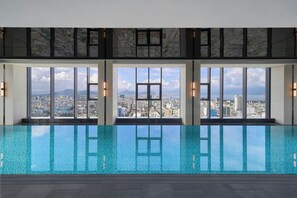 A modern indoor swimming pool with large windows offering city views. - Marriott Executive Apartments Danang, Han River (Da Nang)