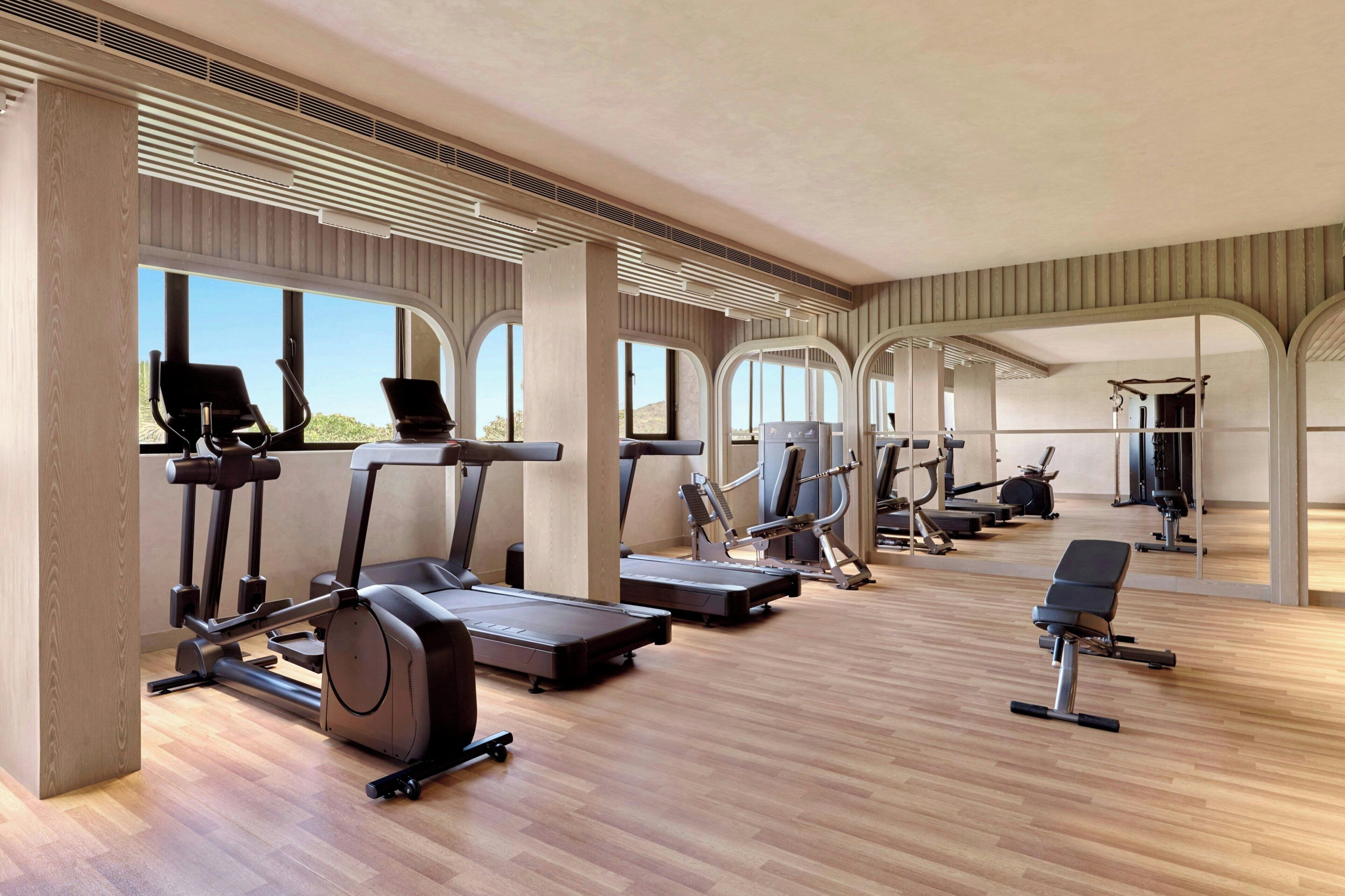 A spacious gym with various exercise equipment, large windows, and a modern architectural design.