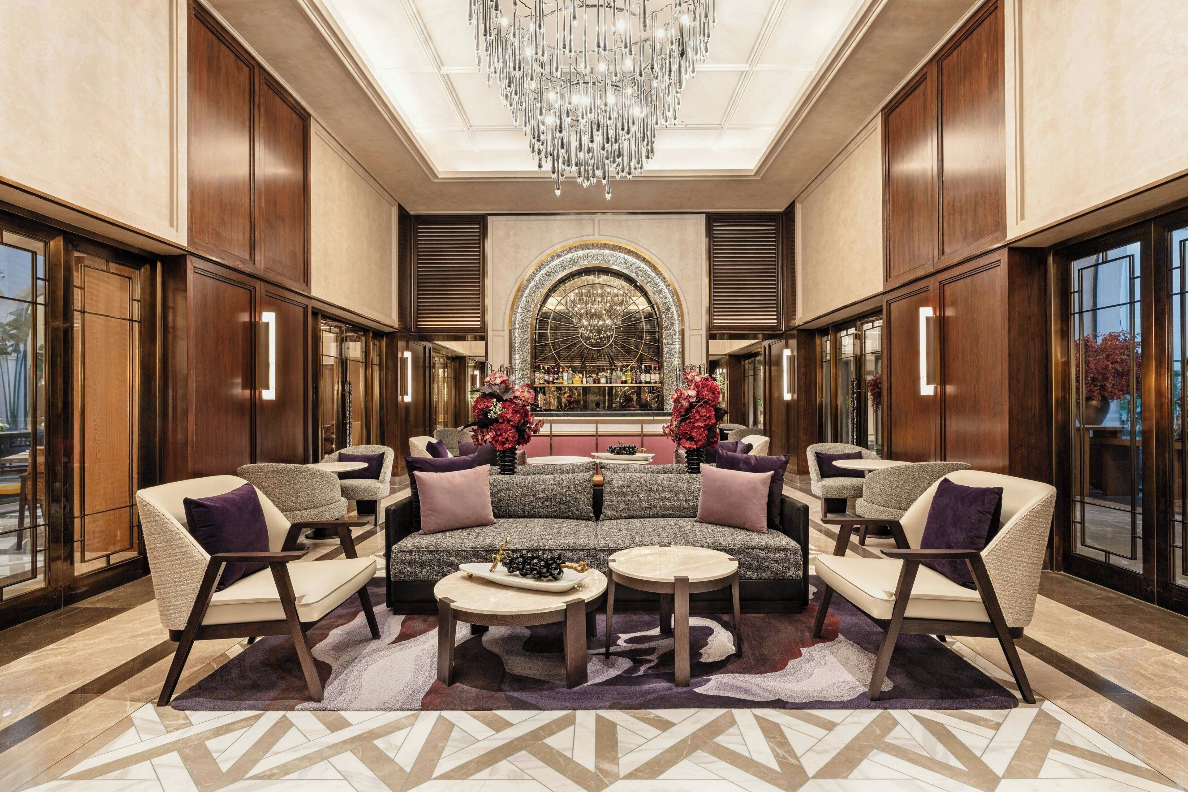 A luxurious lobby with a grand chandelier, a central sofa set, and a decorative arched window.