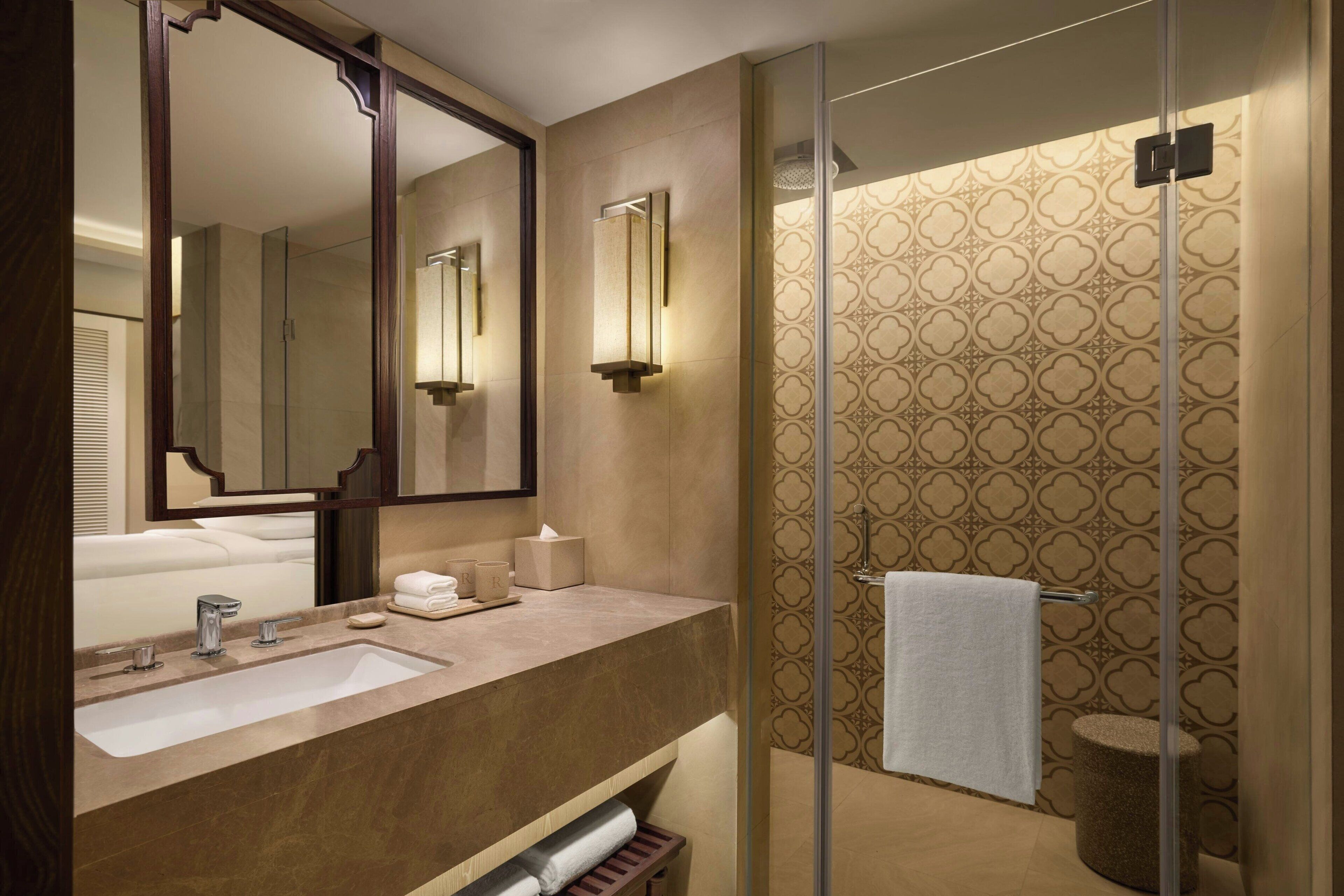 Une salle de bain moderne avec un grand miroir, deux vasques, une douche à l’italienne et un papier peint à motifs.