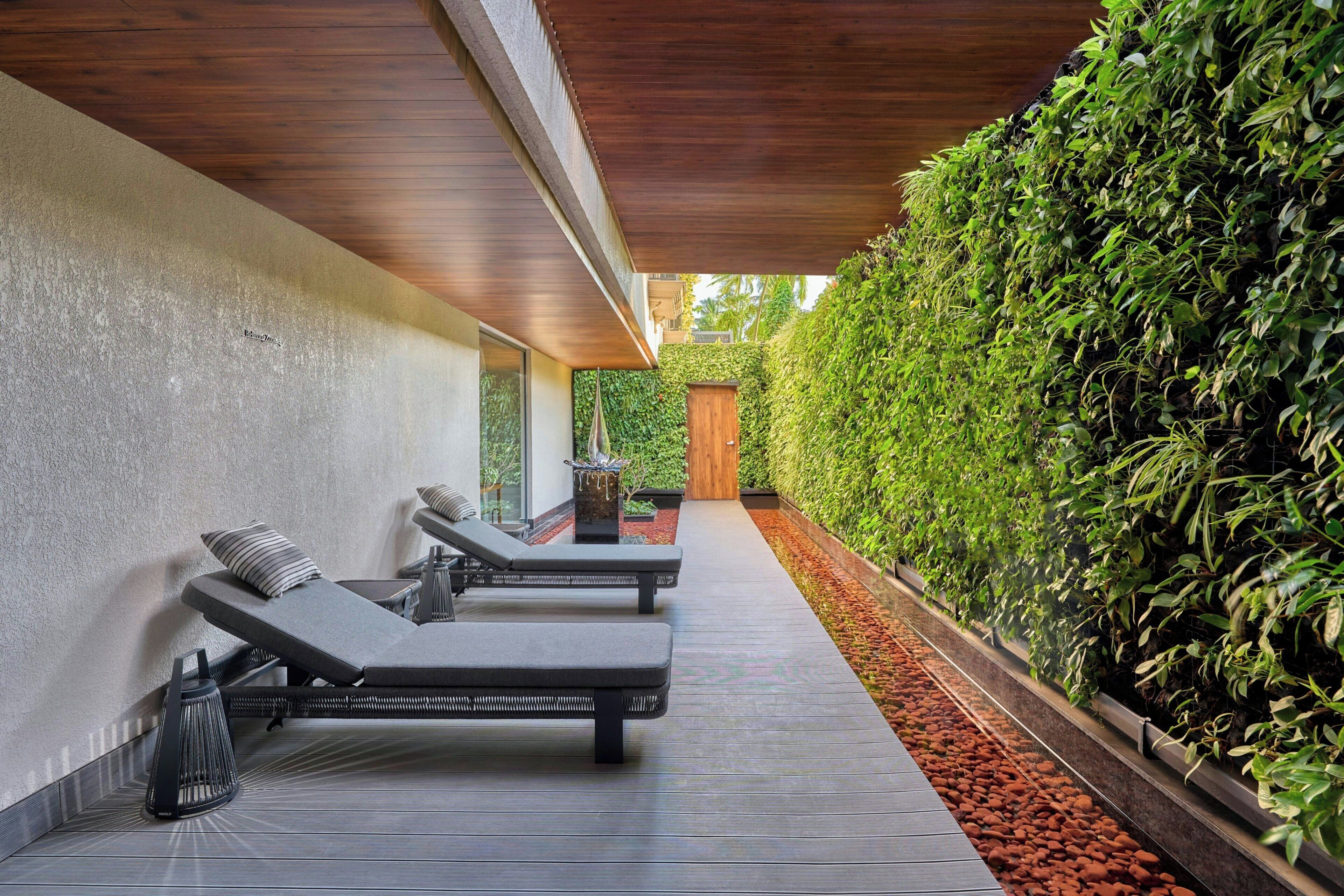 A modern outdoor lounge area with sun loungers, a wooden ceiling, and a vertical garden wall.