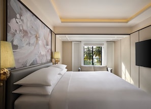 A hotel room with a large bed, a wall-mounted TV, a window with shutters, and a painting on the wall.