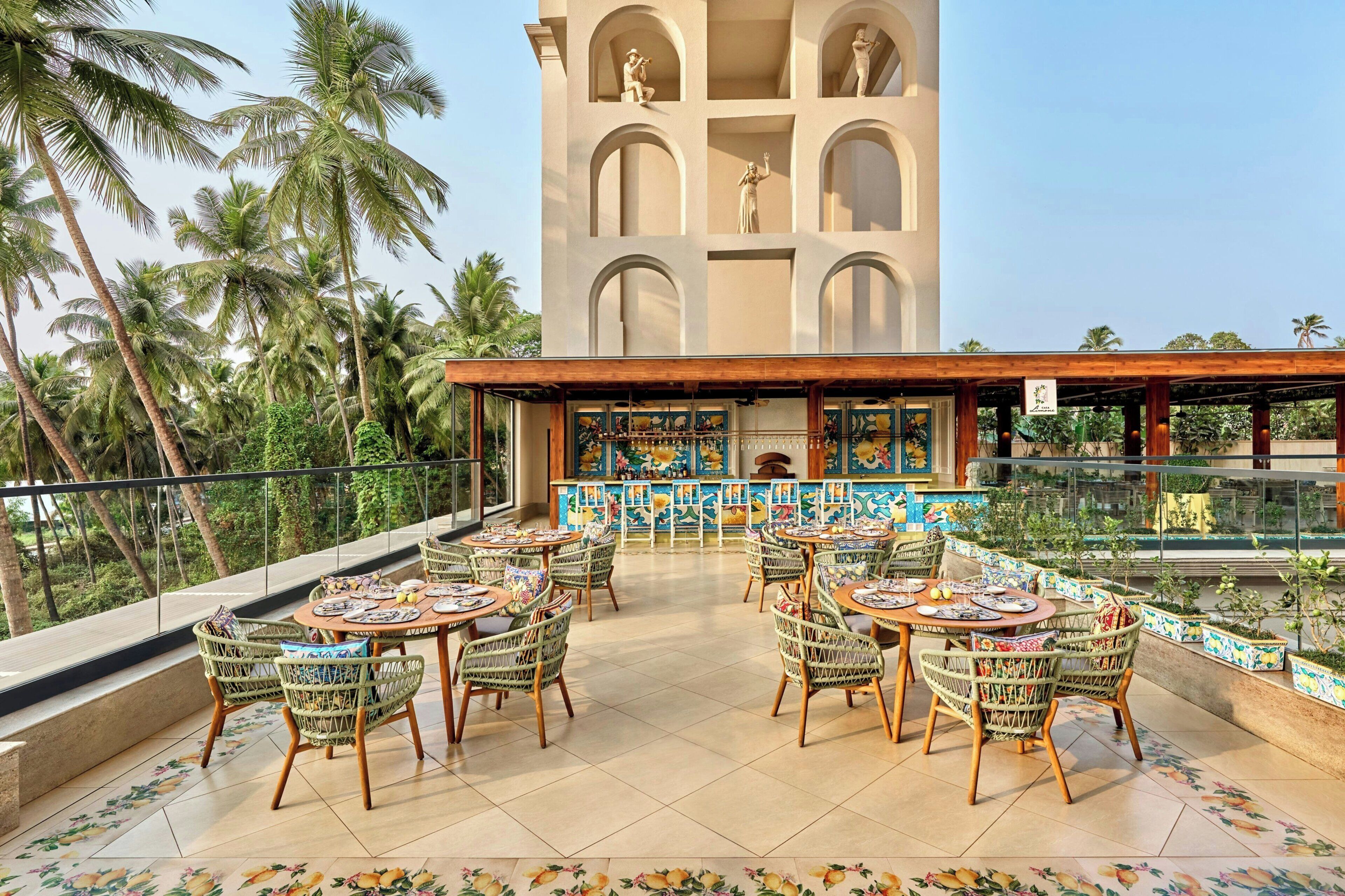 A rooftop terrace with outdoor seating, a view of palm trees, and a building with arched windows.
