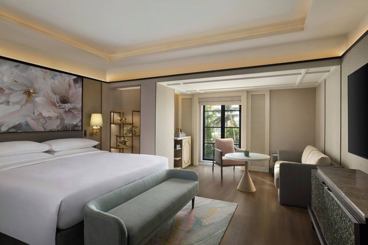 Ein Hotelzimmer mit einem großen Bett, einer Sitzbank, einem Schreibtisch, einem Stuhl und einem Fernseher.