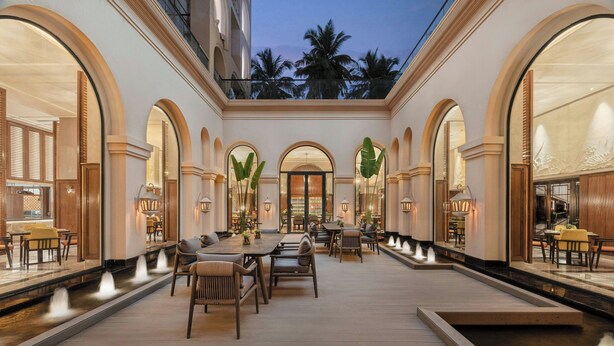 A spacious indoor area with a long table and chairs, a water feature, and large arched windows. - Renaissance Goa Hotel (Arpora)