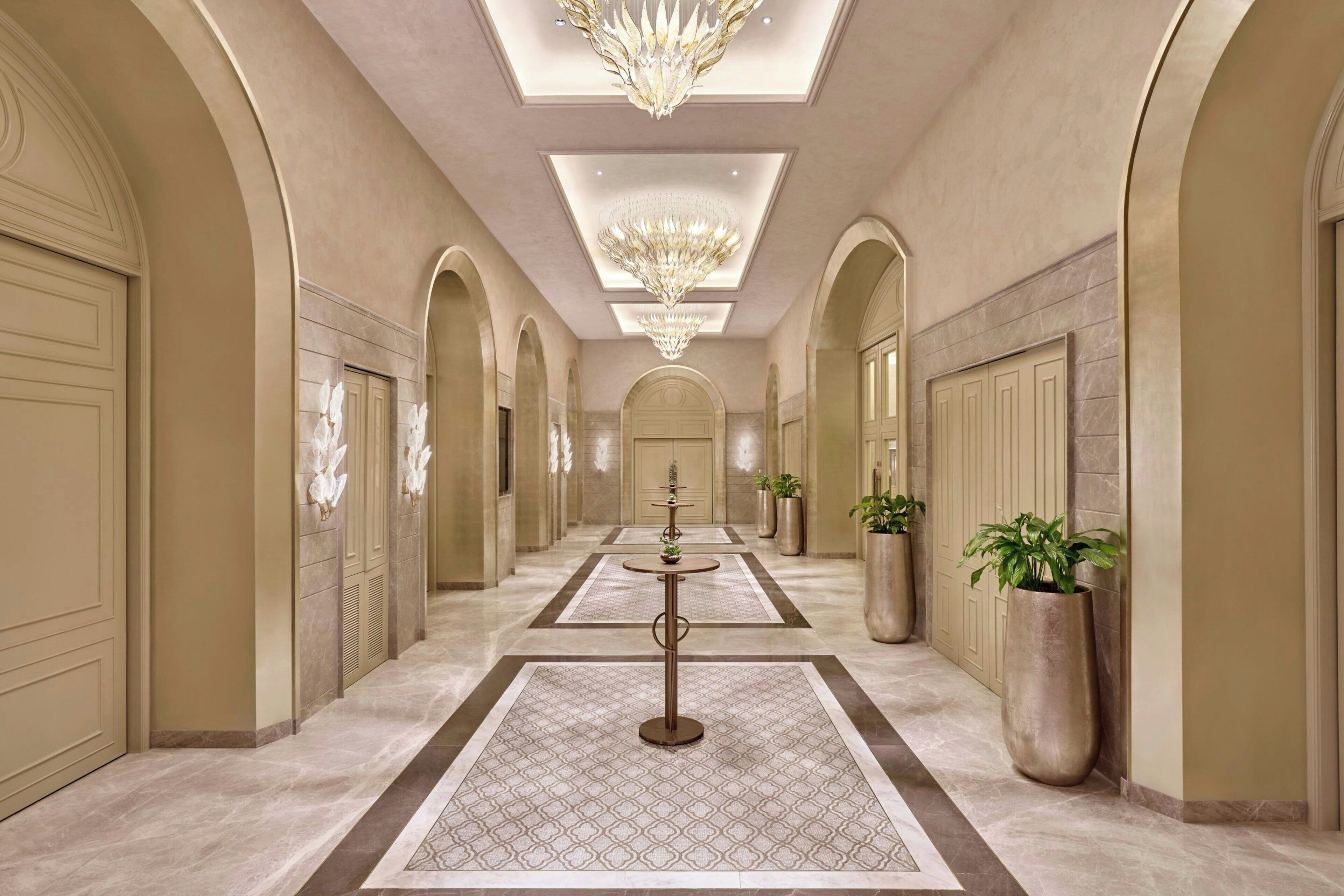 A hallway with arched ceilings, chandeliers, and potted plants.