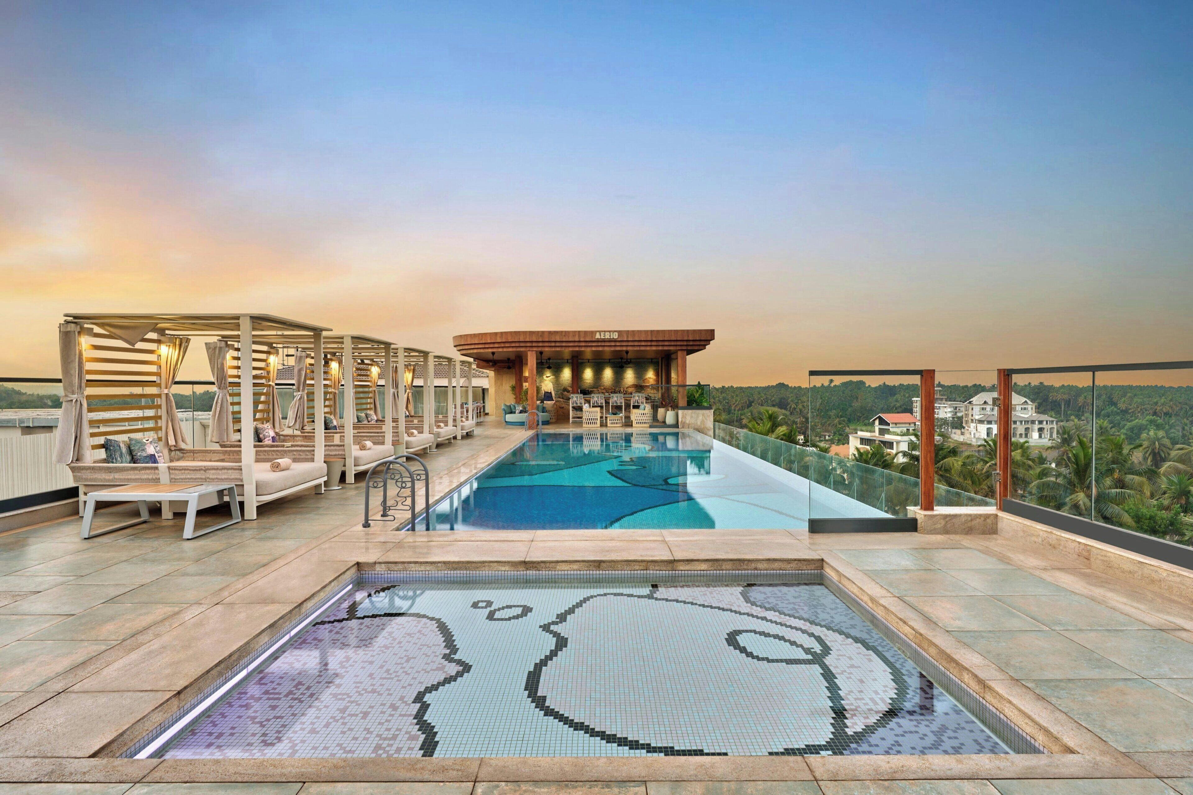 A rooftop infinity pool with a view of the city, a lounge area with sun loungers, and a building labeled 'AERIO'.