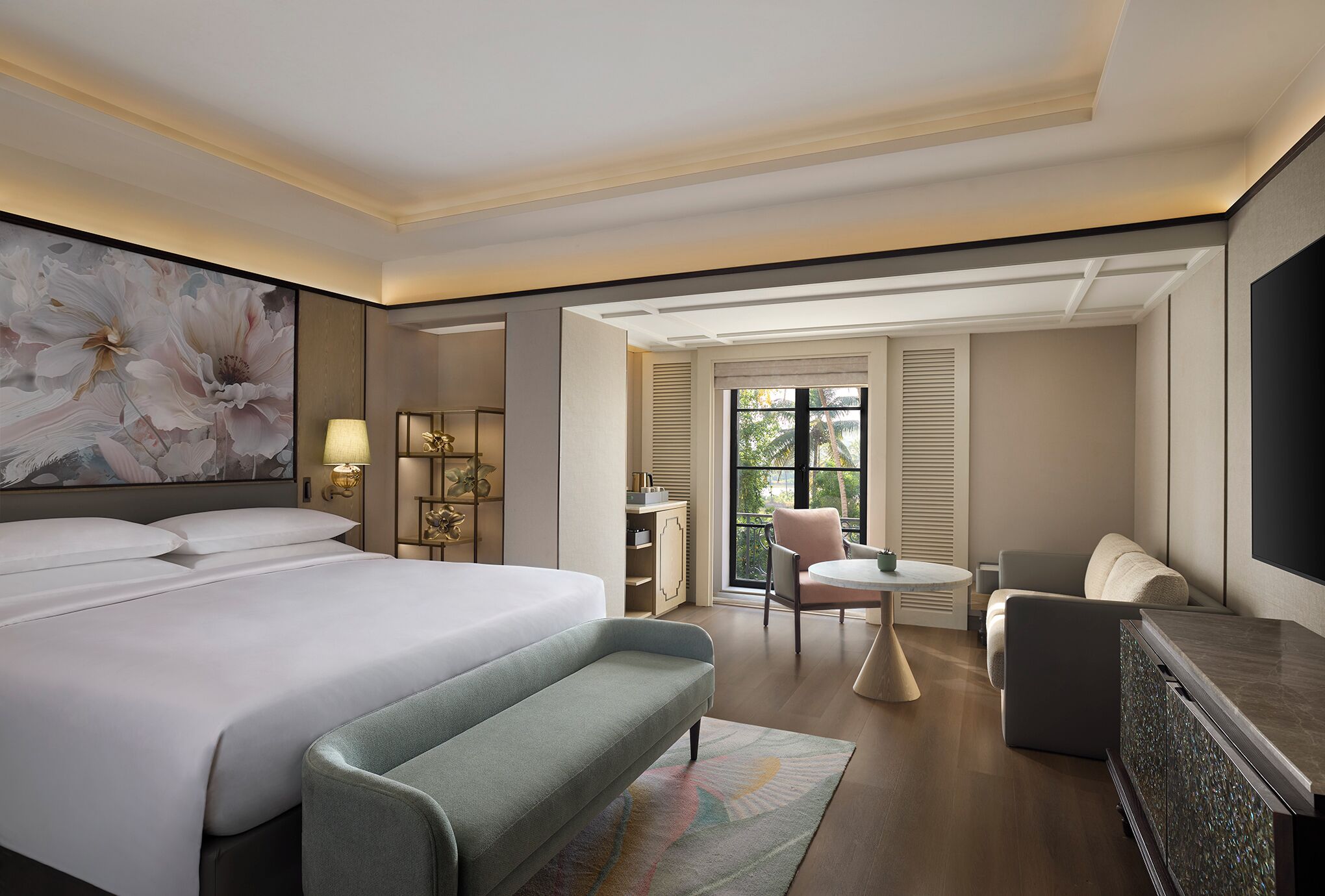 Une chambre d’hôtel dotée d’un grand lit, d’un coin salon avec une table et des chaises, d’une télévision et d’une grande fenêtre avec des volets.